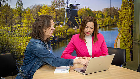 Twee vrouwen zitten aan tafel achter een laptop