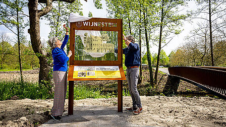 Twee personen onthullen het bord van kasteel Wijnestein