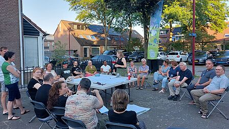 Groep mensen zit buiten om een tafel in een woonwijk