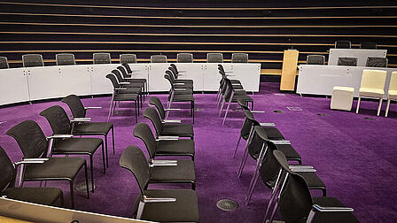 Zaal met paarse vloerbedekking en opstelling met stoelen