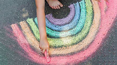 Kind maakt regenboog met stoepkrijt