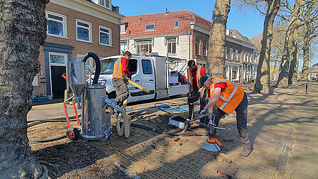 Drie mannen spuiten met een apparaat lucht in de grond bij een boom