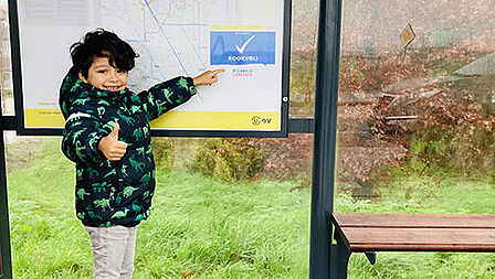 Jongetjes steekt duim op en wijst rookvrij-sticker aan in bushalte