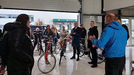 Man spreekt voor een groep mensen met fiets in een open bedrijfsruimte