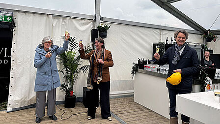 Drie mensen houden lachend een glas bubbels omhoog in een tent