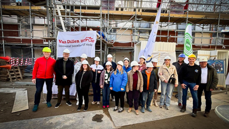 Groep mensen met bouwhelmen staan voor een gebouw in aanbouw