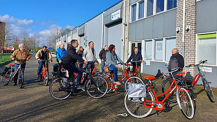 Groep mensen met fiets voor een bedrijfspand