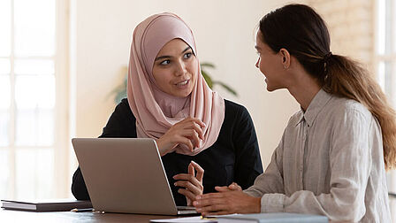 Twee vrouwen praten met elkaar achter een laptop