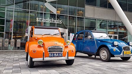 Twee oude 2CV auto's staan ge[parkeerd voor het Stadshuis