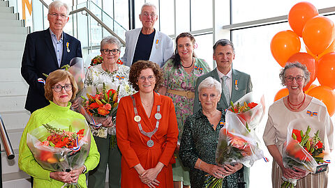 Groep mensen en burgemeester Marijke van Beukering voor een trap met oranje ballonnen
