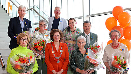 Groep mensen en burgemeester Marijke van Beukering voor een trap met oranje ballonnen