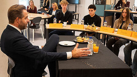 Minister Hugo de Jonge aan een tafel voor leerlingen