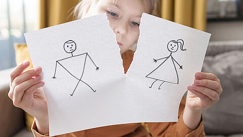 Kind houdt vel papier voor zich met scheur tussen een tekening van een mannetje en een tekening van een vrouwtje